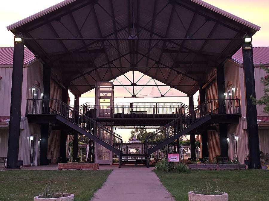Looking straight through the steel pavilion between the two studio wings at dusk: twin stairways to the upper walkway, a pink sky through the far end.