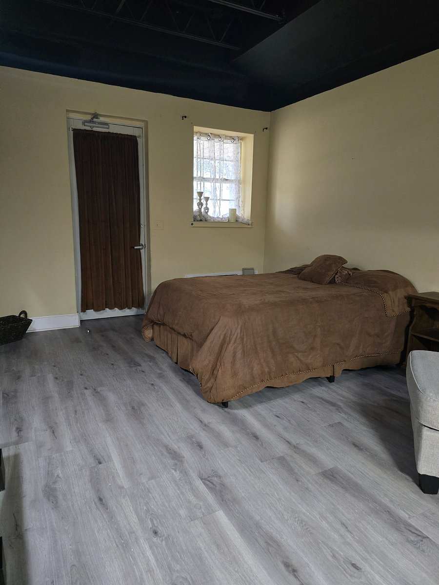 Studio 105: a bed with a brown spread under a black ceiling, a curtained door and a window.