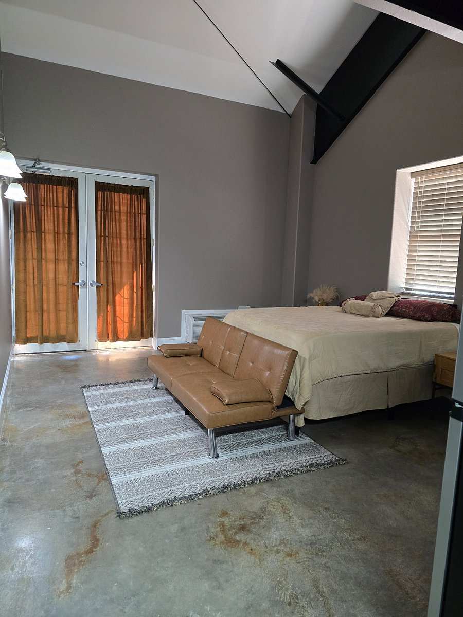 Studio 204: a made-up bed, a tan leather futon on a striped rug, and French doors with rust-coloured curtains.